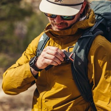 Hiker in a yellow jacket buckling the sternum strap of a Gregory Paragon 60