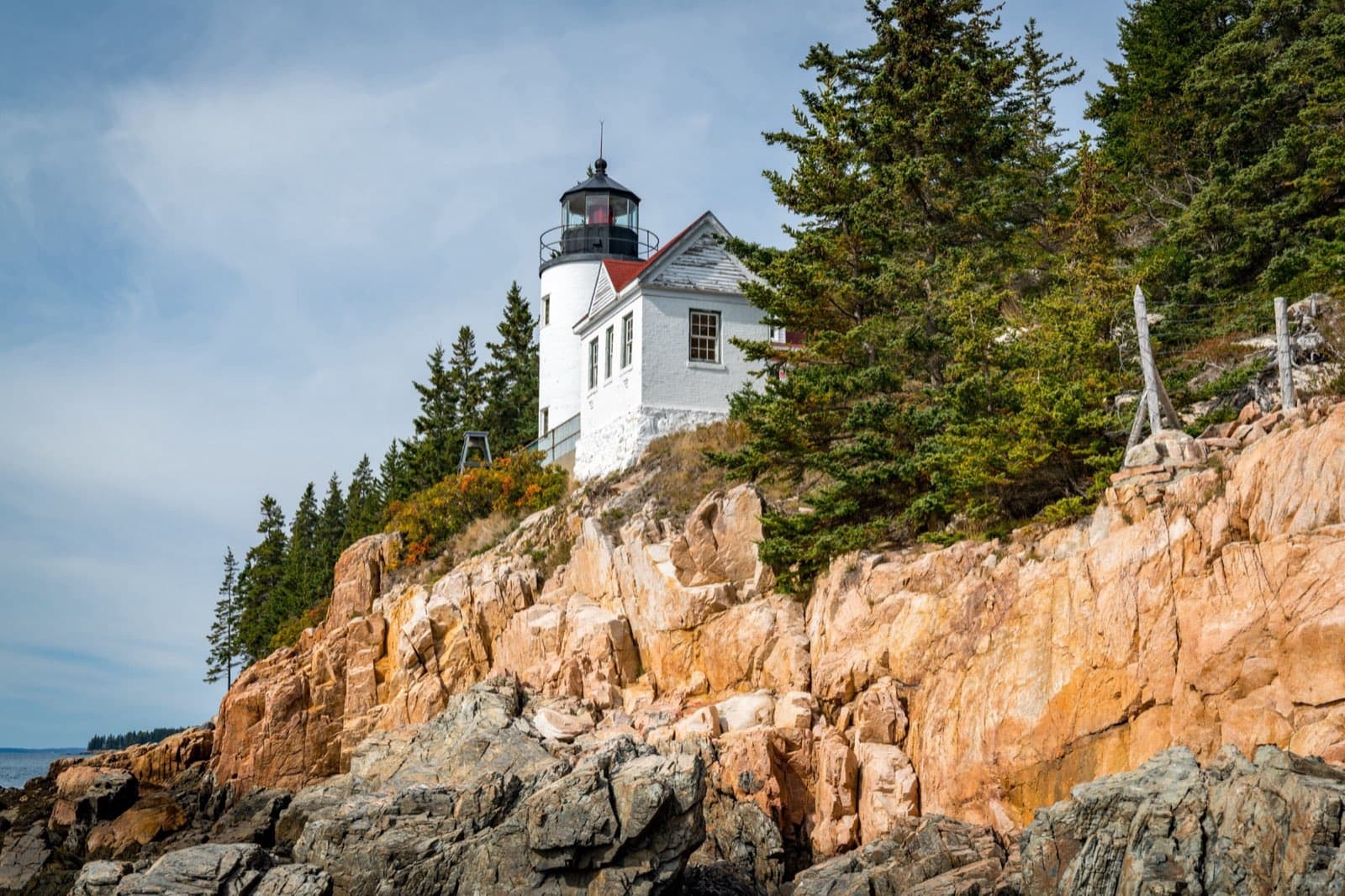 Bass Harbor Head Light Station, the iconic white lighthouse perched on the pink granite cliffs of Acadia National Park's rocky Maine coastline, with evergreens and the Atlantic Ocean.