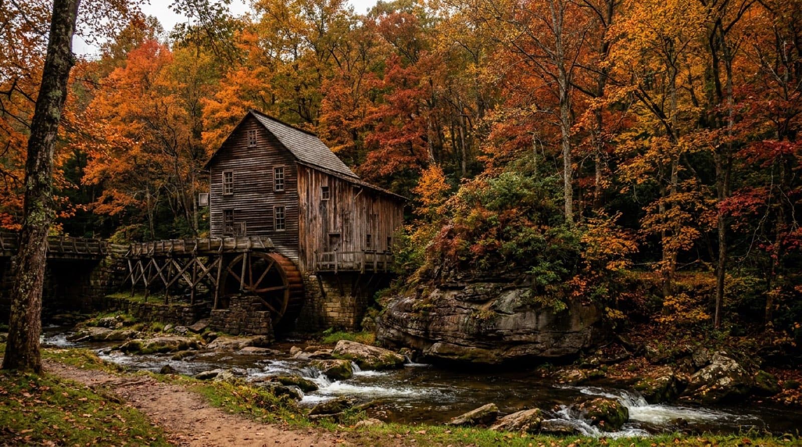 The iconic Glade Creek Grist Mill, a weathered wooden water mill on a rocky creek, framed by brilliant orange and red autumn foliage at peak fall color, water cascading past the mill, West Virginia