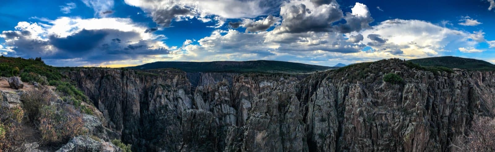 The steep, dark canyon walls of Black Canyon of the Gunnison National Park glowing in golden sunset light, with the deep gorge of the Gunnison River cut into ancient Colorado rock.