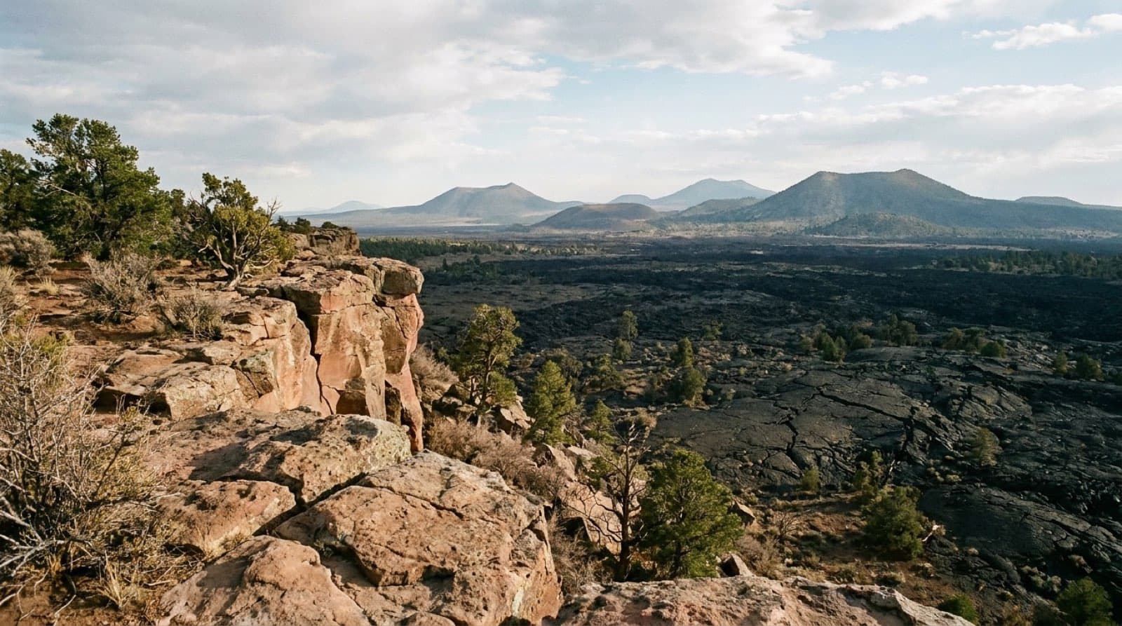 View from the Sandstone Bluffs Overlook across a vast rugged black lava flow toward distant volcanic cones at El Malpais National Monument