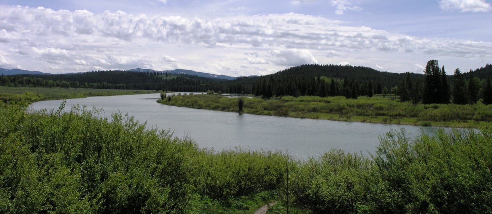 The Teton Range rising behind a calm meander of the Snake River at Oxbow Bend in Grand Teton National Park, Wyoming, with forested banks and snow-flecked peaks reflected in the water