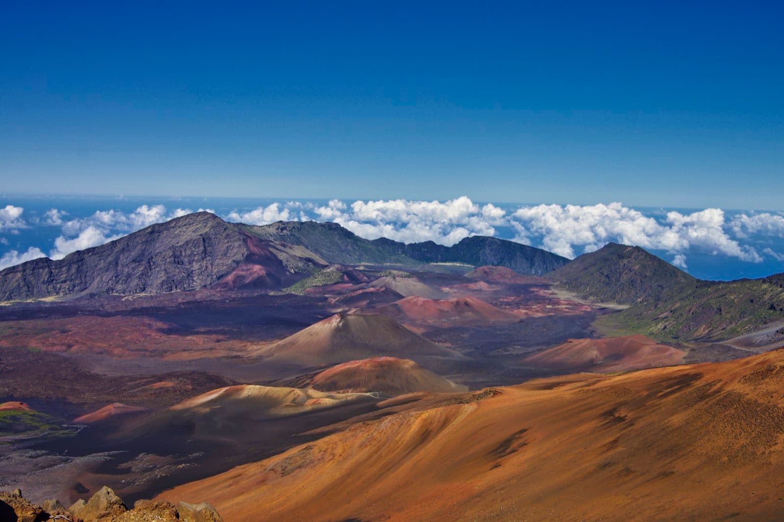 The volcanic crater of Haleakala National Park on Maui, Hawaii, a vast reddish-brown basin of cinder cones and barren lava under a clear sky, viewed from the summit at nearly 3,000 meters elevation