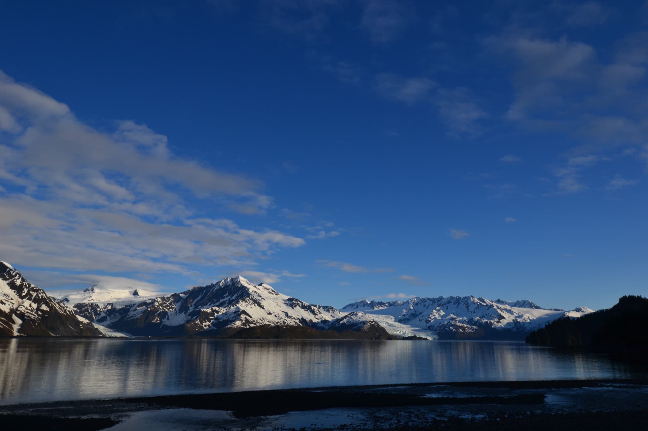 Early morning light over the icy expanse of Pedersen and Aialik Glaciers descending toward the water in Kenai Fjords National Park, Alaska, framed by surrounding coastal mountains.