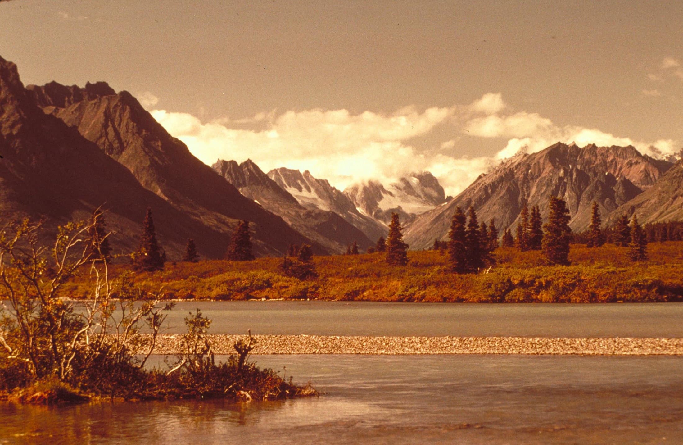 Wide landscape view across Lake Clark National Park and Preserve in Alaska, showing the long glacial lake set among forested foothills and snow-dusted mountains under an open sky.