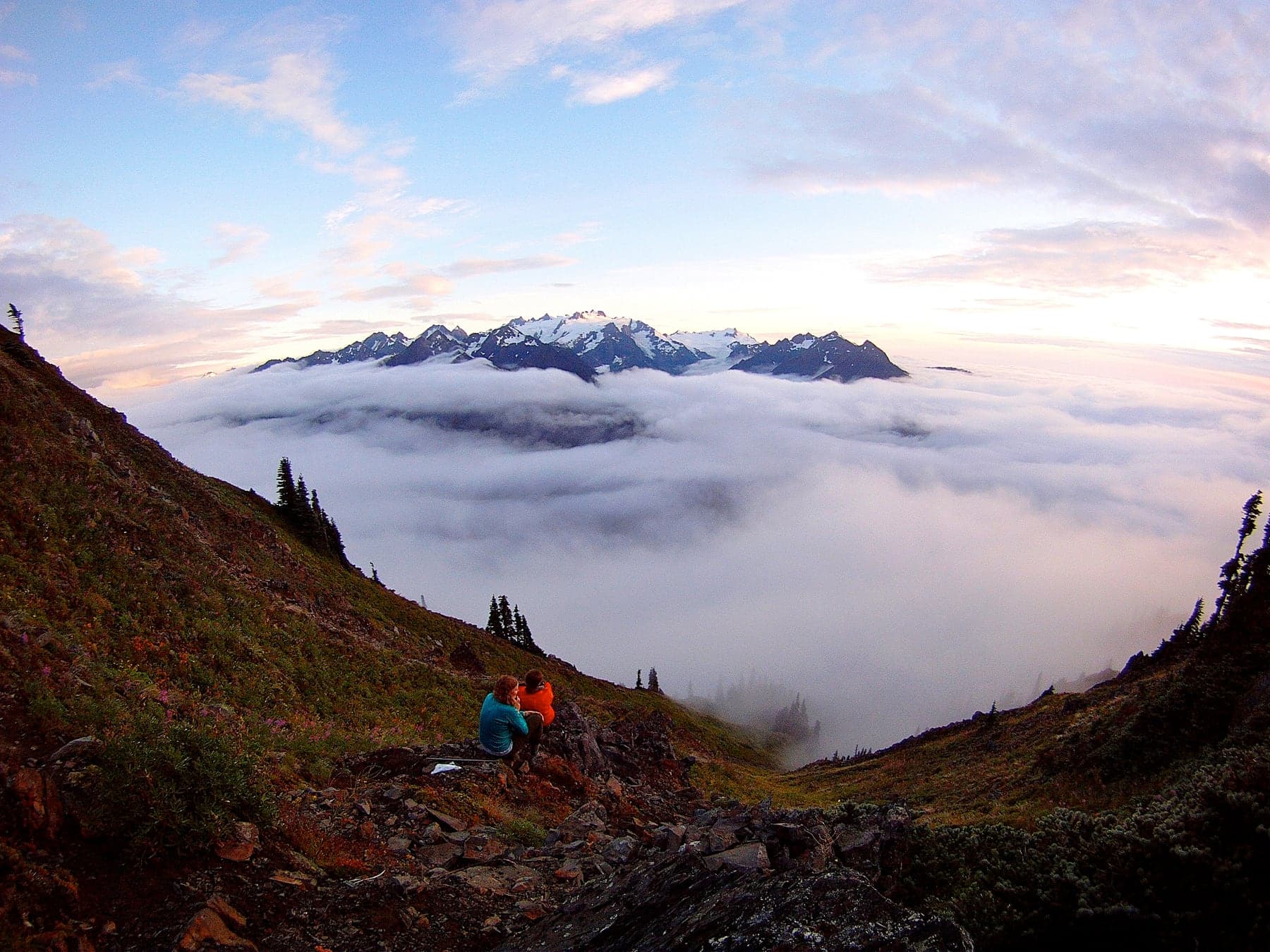 Hikers watching sunset behind snow-capped Olympic Mountains