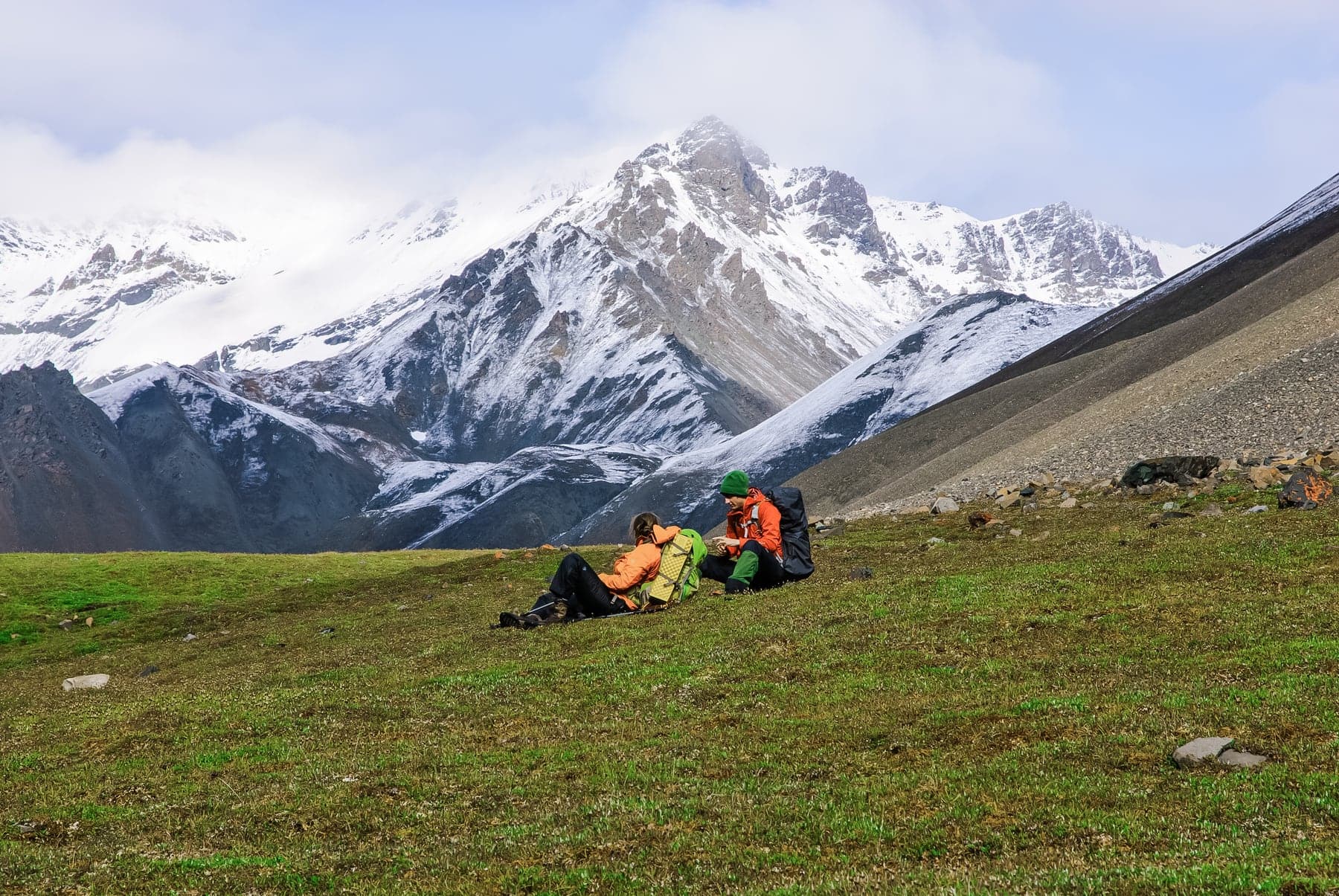 Backpackers sitting in alpine meadow below snowy Mentasta Mountains