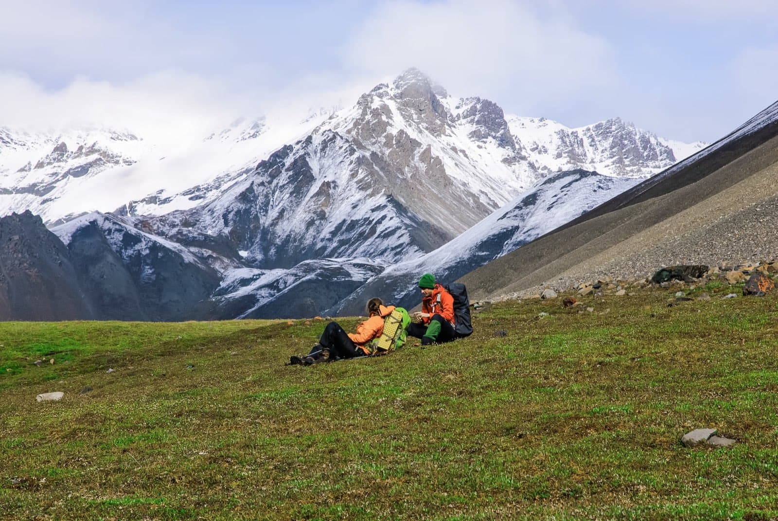 Backpackers sitting in alpine meadow below snowy Mentasta Mountains