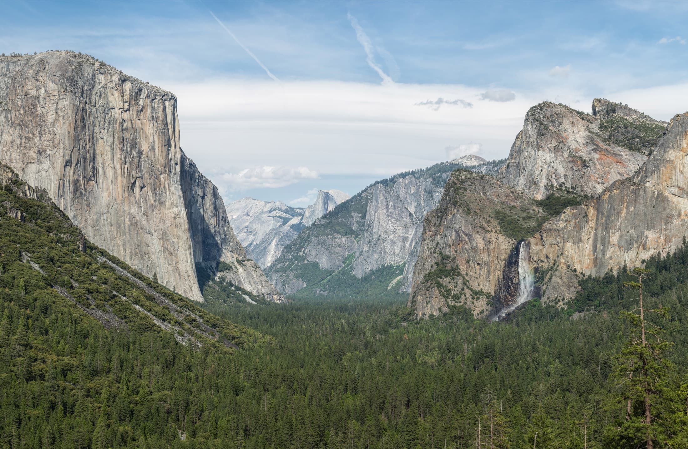 Yosemite Valley seen from Tunnel View, with El Capitan rising on the left, Bridalveil Fall on the right, and Half Dome in the distance under a clear sky