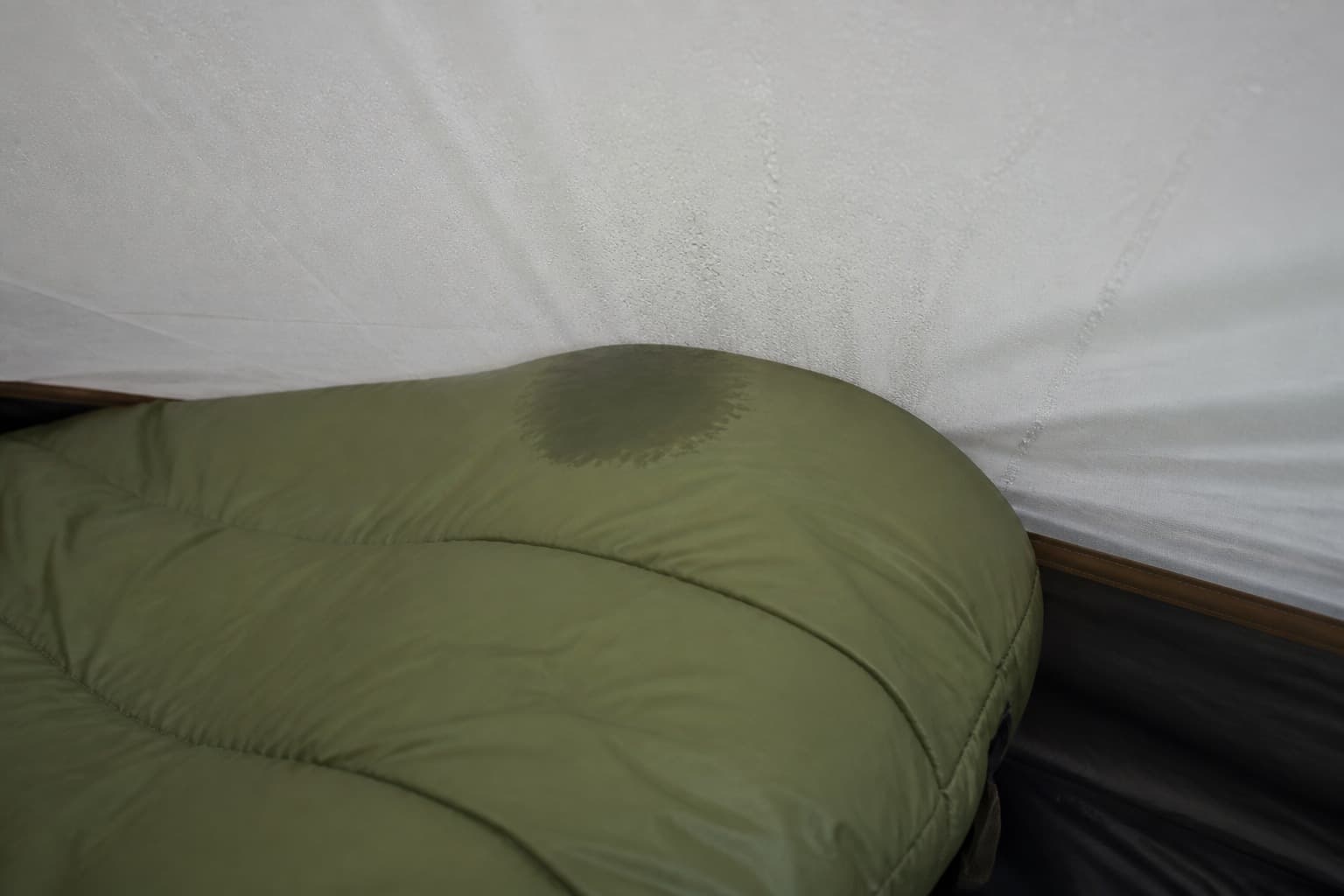 A sleeping bag footbox touching a condensation-covered tent wall with a localized damp patch