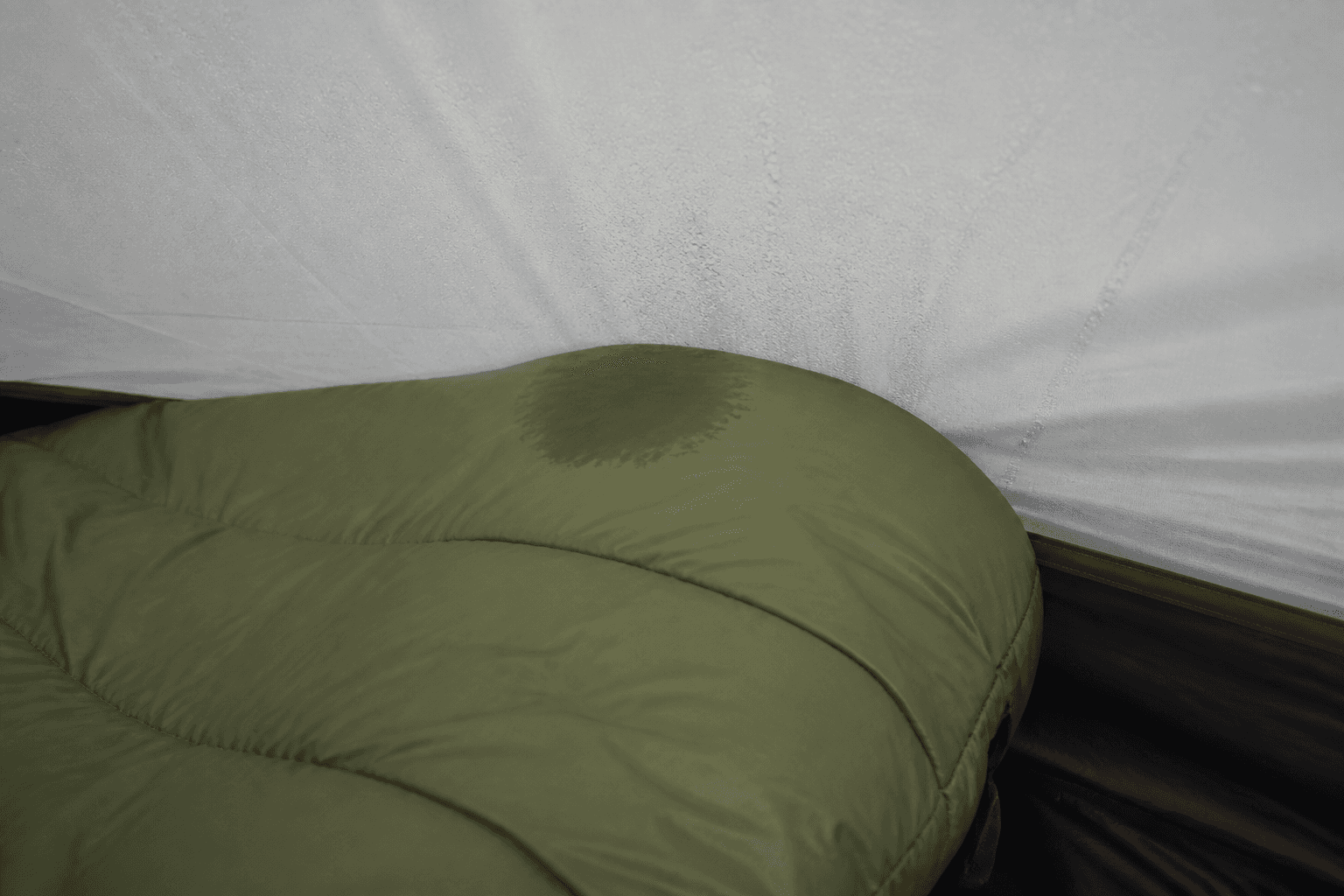 A sleeping bag footbox touching a condensation-covered tent wall with a localized damp patch