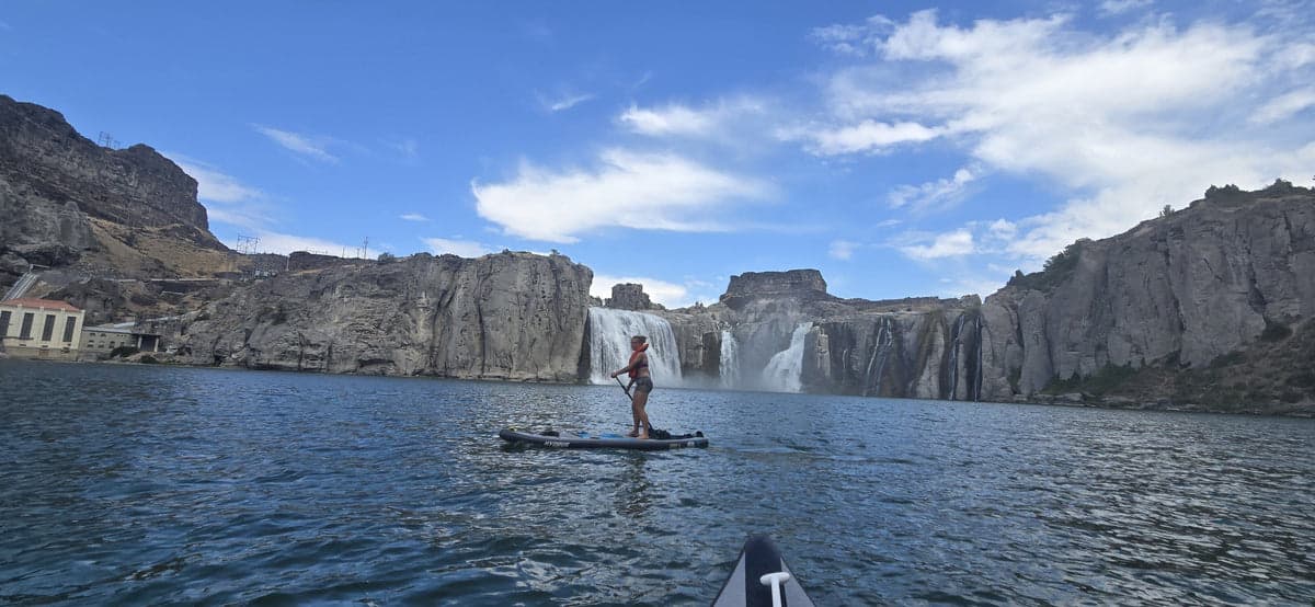 Hydrus manufacturer photograph of a paddleboarder on the water below rocky cliffs and waterfalls