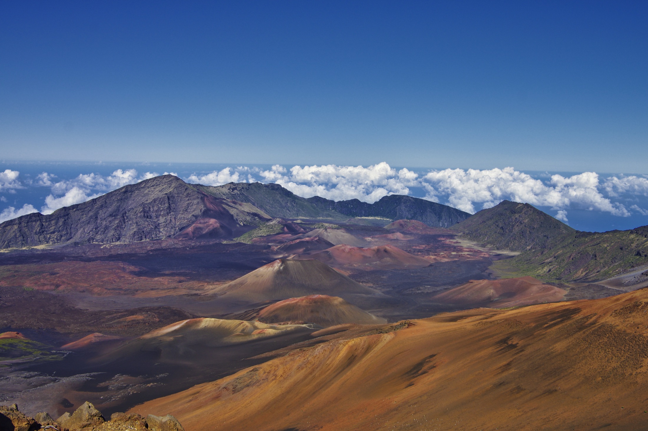 The volcanic crater of Haleakala National Park on Maui, Hawaii, a vast reddish-brown basin of cinder cones and barren lava under a clear sky, viewed from the summit at nearly 3,000 meters elevation