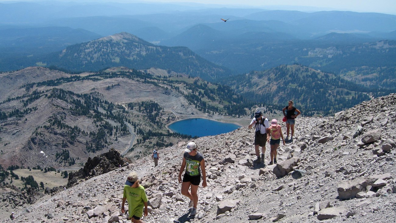 Hikers climbing the Lassen Peak Trail above alpine lakes and volcanic peaks