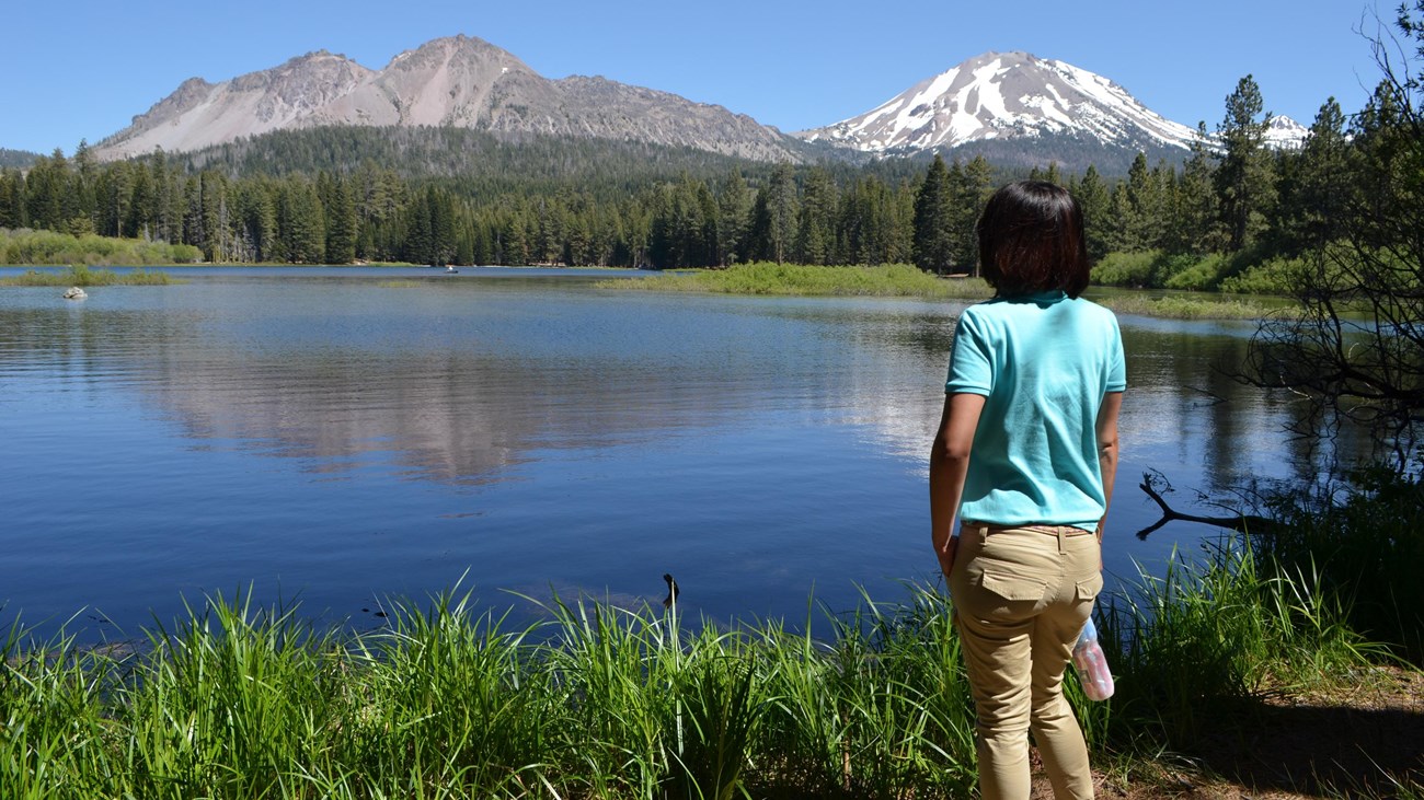 Brush-lined Manzanita Lake with volcanic peaks beyond