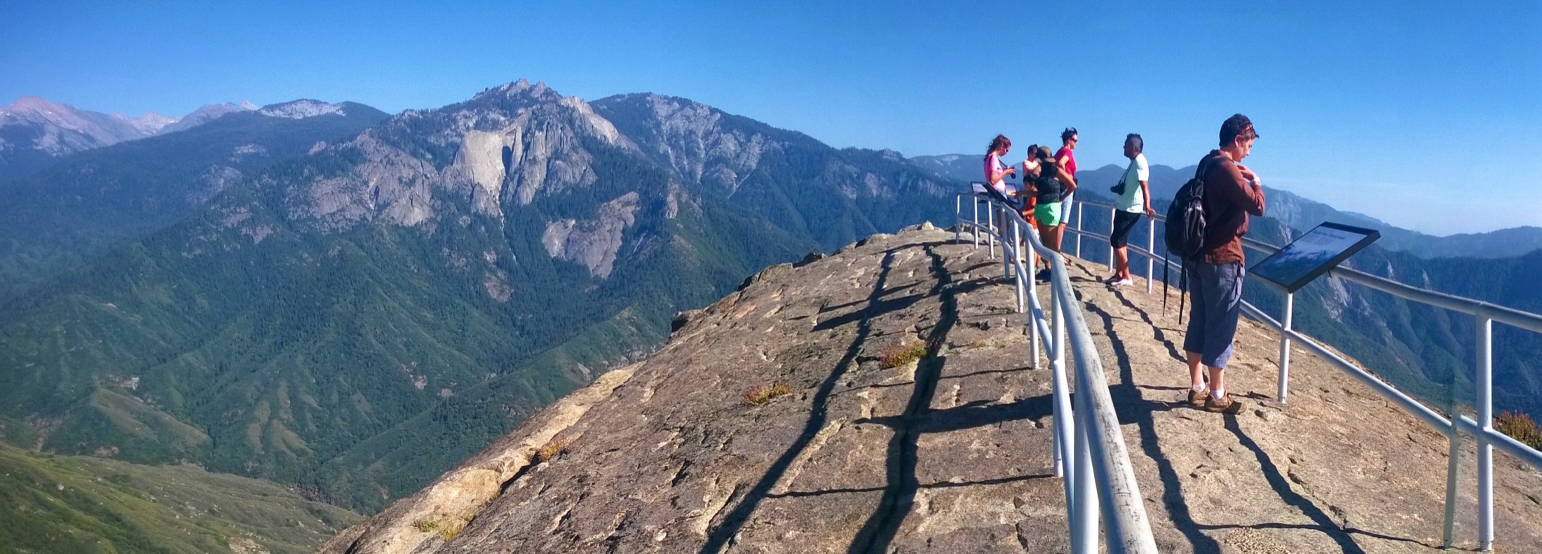 Wide panoramic view from the summit of Moro Rock in Sequoia National Park, looking out over the granite formations of Castle Rocks and Paradise Peak amid forested Sierra Nevada ridgelines under a clear sky.