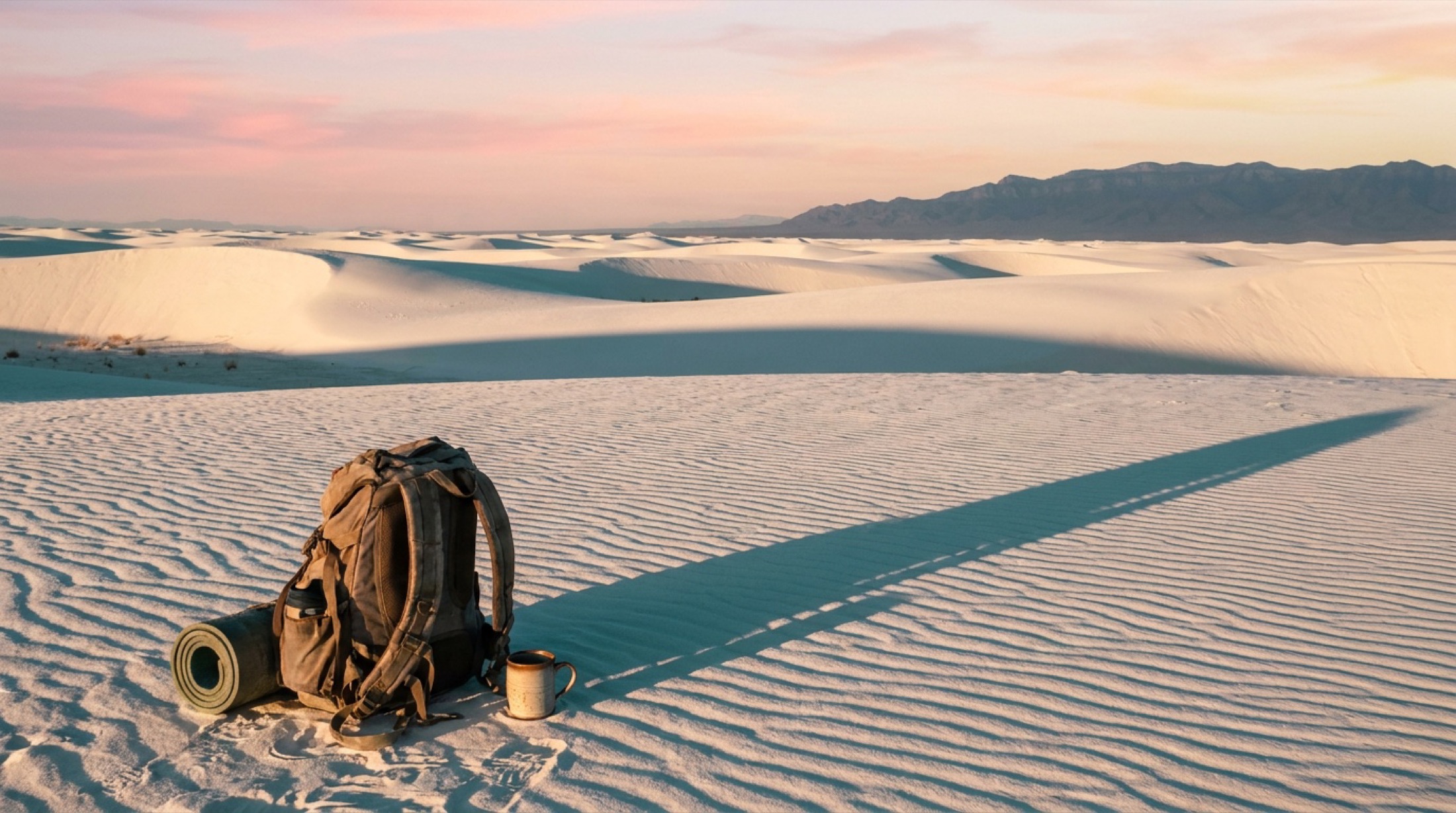 Rolling white gypsum dunes of White Sands at sunset with long blue shadows and a pink sky.