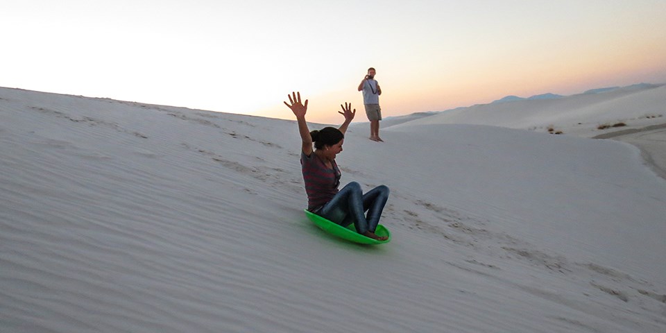 A visitor riding a sled down a gypsum dune